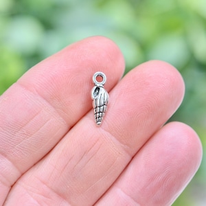 May include: Silver charm in the shape of a seashell with a loop at the top for attaching to jewelry.