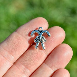 Puede incluir: Encanto de plata en forma de dos bastones de caramelo atados juntos. El encanto es pequeño y sería adecuado para la elaboración de joyas.