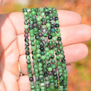 May include: A strand of green and black gemstone beads. The beads are round and have a smooth, polished finish.