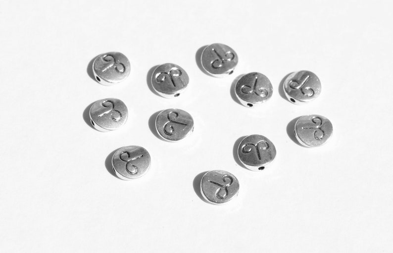 May include: A collection of silver-toned metal beads with the astrological symbol for Aries engraved on each bead.
