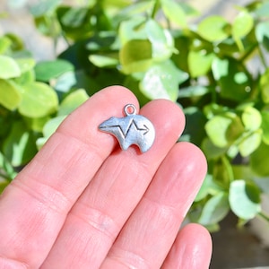 May include: Silver charm in the shape of a bear with a heartbeat and arrow design.