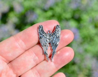 May include: Silver angel wings charm with a detailed design. The wings are open and have a textured surface.