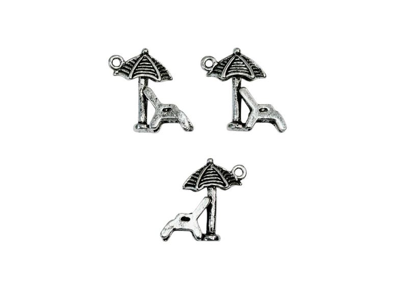 May include: Three silver charm pendants featuring a beach chair and umbrella. The charms are detailed with a textured finish and have a loop for attaching to a bracelet or necklace.