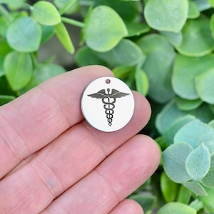 May include: A silver round charm with a medical symbol, the caduceus, a snake wrapped around a staff with wings.