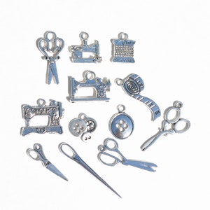 May include: A collection of silver-toned metal charms with sewing themes. The charms include a sewing machine, scissors, a spool of thread, buttons, and a measuring tape.