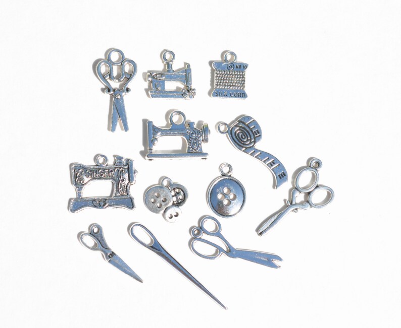 May include: A collection of silver-toned metal charms with sewing themes. The charms include a sewing machine, scissors, a spool of thread, buttons, and a measuring tape.