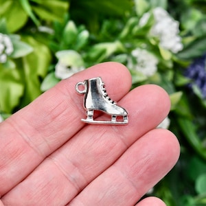 May include: A small, silver-colored ice skate charm with black laces and a loop for attaching to a bracelet or necklace. The charm is detailed and has a vintage aesthetic, perfect for jewelry making or crafting projects.