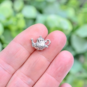 May include: Silver charm in the shape of a teapot with the words "Tea Time" on it.