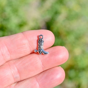 May include: Silver cowboy boot charm with a spur detail. The charm is small and detailed, perfect for adding a western touch to jewellery or crafts.