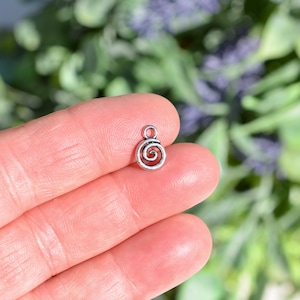 May include: Silver charm with a spiral design. The charm has a loop at the top for attaching to a necklace or bracelet.