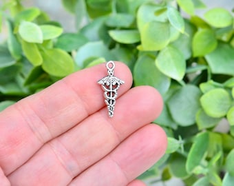 May include: Silver charm in the shape of a medical caduceus, a symbol of medicine, with a snake wrapped around a staff. The charm is detailed and intricate.