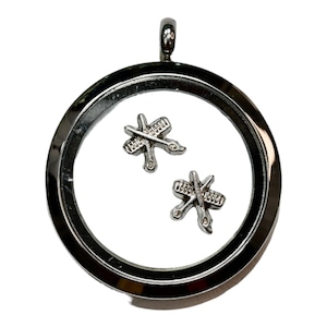 May include: A silver locket necklace with a clear glass insert. Inside the locket are two silver charms shaped like crossed hairdressing scissors and combs.