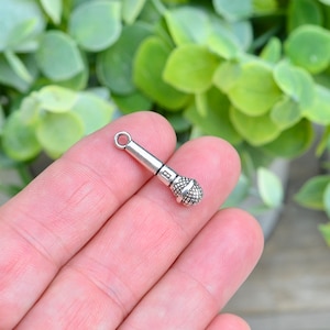 May include: Silver-toned microphone charm with a loop for attaching to a necklace or bracelet.