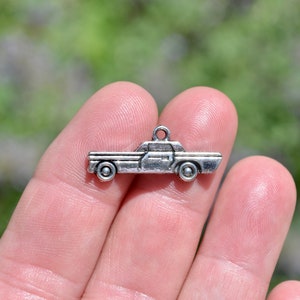 May include: Silver charm in the shape of a vintage car. The charm has a loop at the top for attaching to a necklace or bracelet.