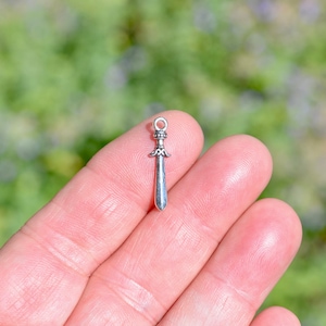 May include: A silver sword charm with a detailed design. The charm is small and would be perfect for adding to a necklace or bracelet.