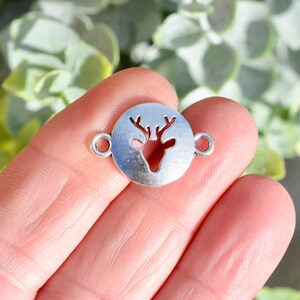 May include: Silver-toned metal charm with a cut-out design of a deer head. The charm has two jump rings for attaching to jewelry or other crafts.