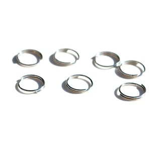 May include: Eight silver jump rings, also known as key rings, are arranged in a scattered pattern on a white background.
