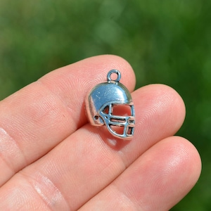 May include: A silver-toned metal charm shaped like a football helmet. The helmet has a face mask and is detailed with a raised design.