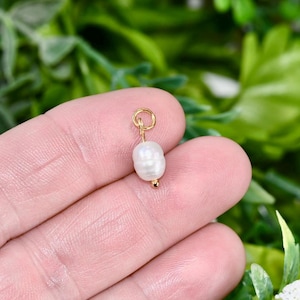 Peut inclure: Un petit charme en perle blanche avec un anneau de saut en or. La perle est attachée à l'anneau de saut avec un fil d'or.