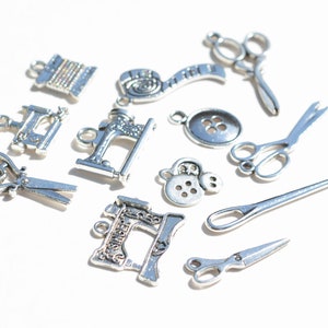 May include: A collection of silver-toned metal charms featuring sewing-themed designs, including scissors, a sewing machine, buttons, and spools of thread.