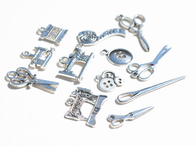 May include: A collection of silver-toned metal charms featuring sewing-themed designs, including scissors, a sewing machine, buttons, and spools of thread.