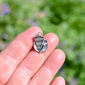 May include: Silver charm featuring a slice of pie on a plate with a fork. The charm is designed to be used for jewelry making.