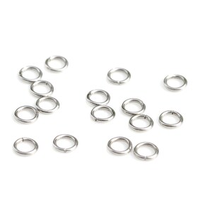 May include: A collection of silver jump rings, scattered on a white background. These rings are used for jewelry making and crafting.