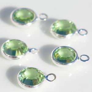 May include: Five silver charms with light green crystal stones. Each charm has a loop for attaching to a necklace or bracelet.