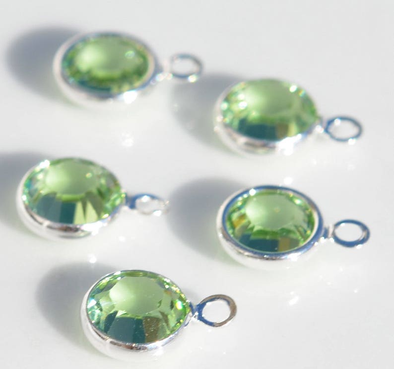 May include: Five silver charms with light green crystal stones. Each charm has a loop for attaching to a necklace or bracelet.
