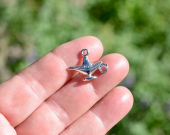 May include: Silver-toned metal charm shaped like an Aladdin's lamp. The charm has a loop at the top for attaching to a necklace or bracelet.