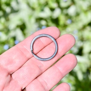 May include: A silver key ring, held in a hand, against a blurred green background.