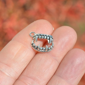 May include: Silver charm in the shape of a set of teeth, with sharp points, resembling a predator's mouth.
