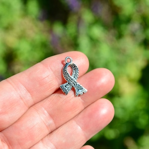 May include: Silver charm in the shape of a ribbon with a braided design.