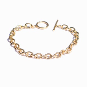 May include: A gold chain bracelet with a toggle clasp. The chain is made of thick, oval-shaped links.
