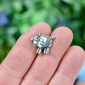 May include: Silver charm in the shape of a sheep. The sheep has a detailed face and a fluffy body.