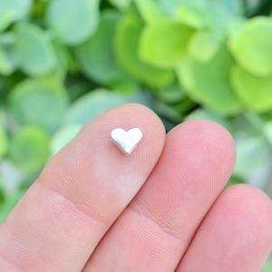 May include: A small silver heart charm, held between two fingers.