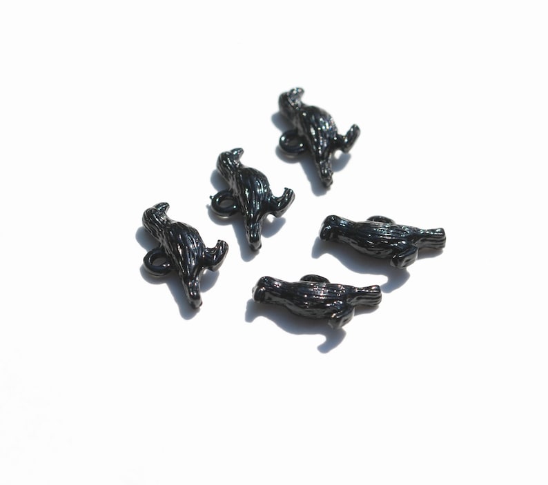 May include: Five black plastic buttons shaped like birds. The buttons have a textured surface and are designed to look like a bird in flight.