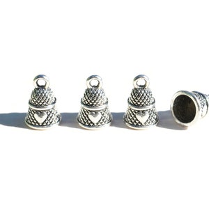 Peut inclure: Quatre breloques en forme de d&eacute; &agrave; coudre en m&eacute;tal argent&eacute; dispos&eacute;es en ligne. Chaque breloque pr&eacute;sente un motif textur&eacute; en croisillons, un petit c&oelig;ur en relief sur le c&ocirc;t&eacute; et une boucle circulaire au sommet pour la fixation.
