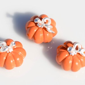May include: Three small orange ceramic pumpkins with silver accents. The pumpkins have a ribbed texture and are decorated with a silver stem and leaf.