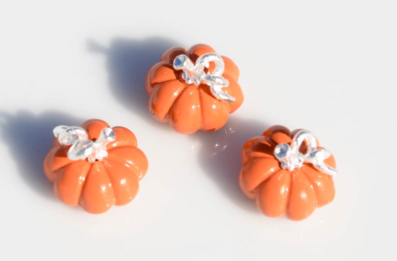 May include: Three small orange ceramic pumpkins with silver accents. The pumpkins have a ribbed texture and are decorated with a silver stem and leaf.