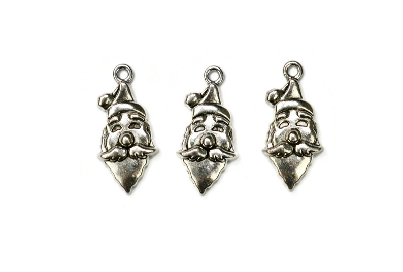 May include: Three silver-toned metal charms shaped like Santa Claus faces. Each charm has a red hat, white beard, and a smiling face.