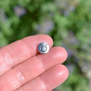 May include: A silver charm with the Taurus zodiac symbol engraved on it.
