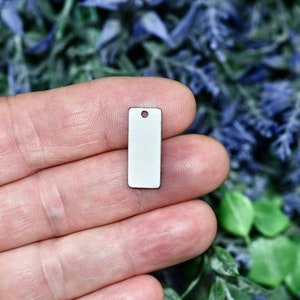 May include: A small, white, rectangular metal tag with a hole at the top. The tag is blank and ready for personalization.