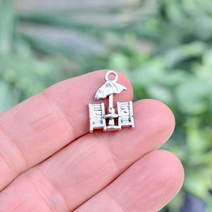 May include: Silver charm featuring a pair of beach chairs with an umbrella. The charm is perfect for adding a summery touch to jewelry.