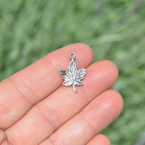 May include: Silver-toned metal maple leaf charm pendant. The leaf is detailed with veins and has a smooth, polished finish.