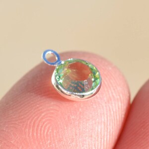 May include: A silver charm with a green gemstone. The charm has a loop for attaching to a bracelet or necklace.