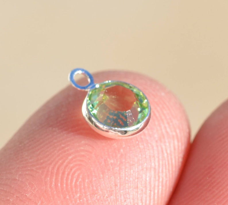 May include: A silver charm with a green gemstone. The charm has a loop for attaching to a bracelet or necklace.