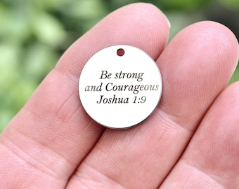 May include: A circular silver-toned metal charm featuring a small hole at the top for attachment. The surface is engraved with the black text "Be strong and Courageous Joshua 1:9" in a serif font, centered on the flat, polished metal disc.