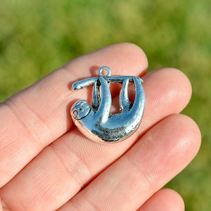 May include: Silver charm of a sloth hanging upside down. The charm is detailed with a face and claws.