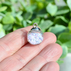 May include: A silver charm with a clear glass sphere filled with iridescent white and pink glitter.